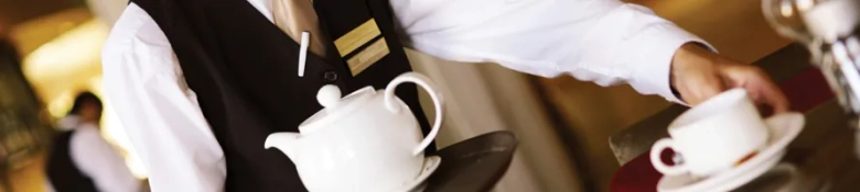 Waiter in uniform serving tea at a restaurant, representing part-time work for university students.