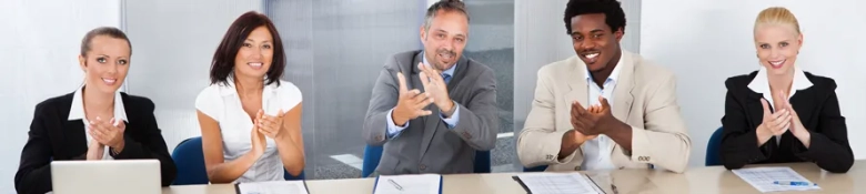 Five professionals seated at a table clapping, possibly after a successful job interview presentation.