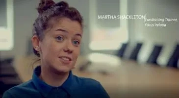 Martha Shackleton in an office setting with her name and title displayed as a fundraising trainee for Focus Ireland.