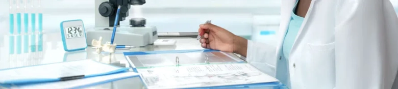 Laboratory setting with a healthcare professional reviewing documents, microscope, and test tubes in the background.