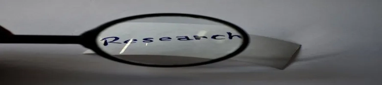 Magnifying glass focusing on the word "Research" written on a piece of paper.