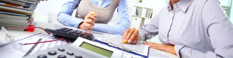 Two people sitting at a table that is covered in calculators