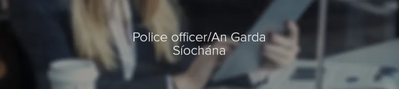 Blurred image of a person in an office setting with the text "Police officer/An Garda Síochána" overlayed.