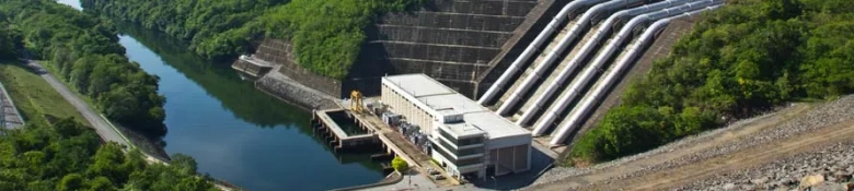 Aerial view of a hydroelectric dam with multiple spillways surrounded by lush greenery.