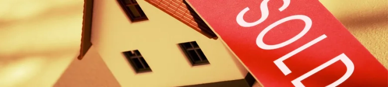 Miniature house model with a red 'SOLD' sign indicating a successful real estate transaction.